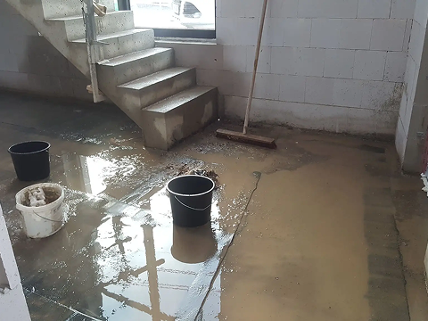 Flooded basement with buckets and a broom.