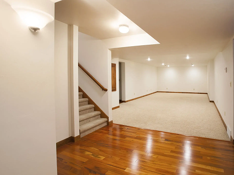 Spacious basement with wooden floor and stairs.