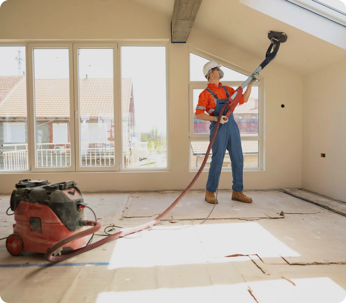 Worker sanding ceiling in unfinished room.