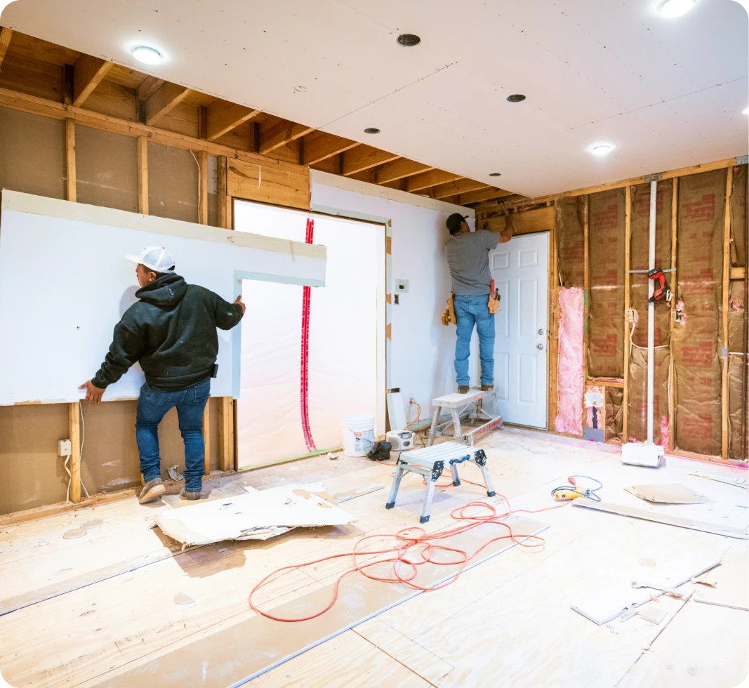 Workers installing drywall in a room renovation.